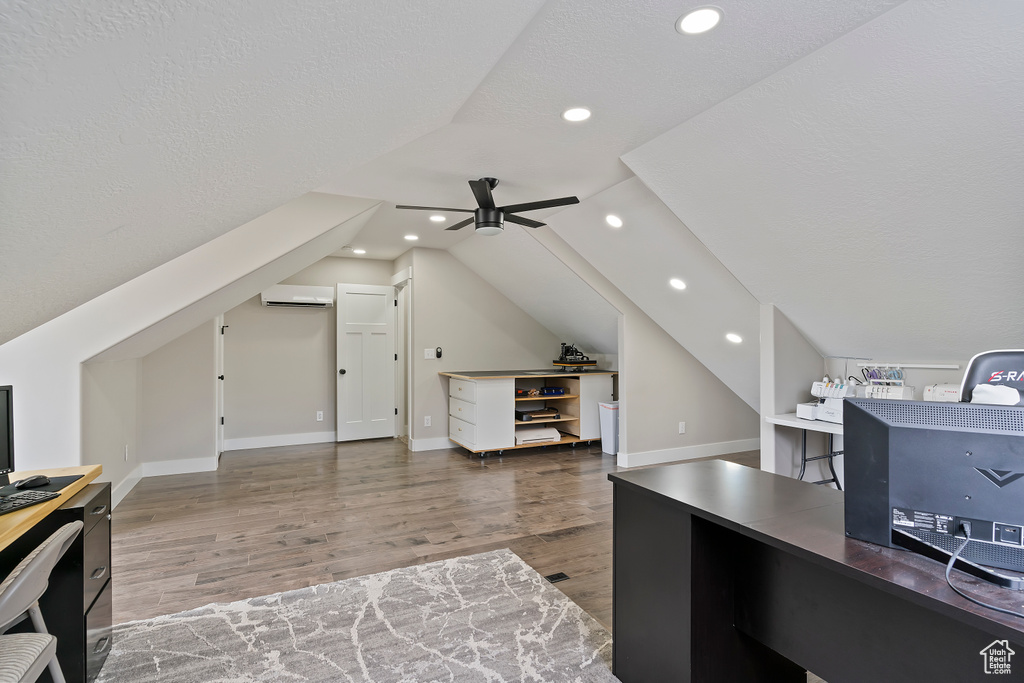 Office area with wood finished floors, a ceiling fan, a wall unit AC, lofted ceiling, and baseboards