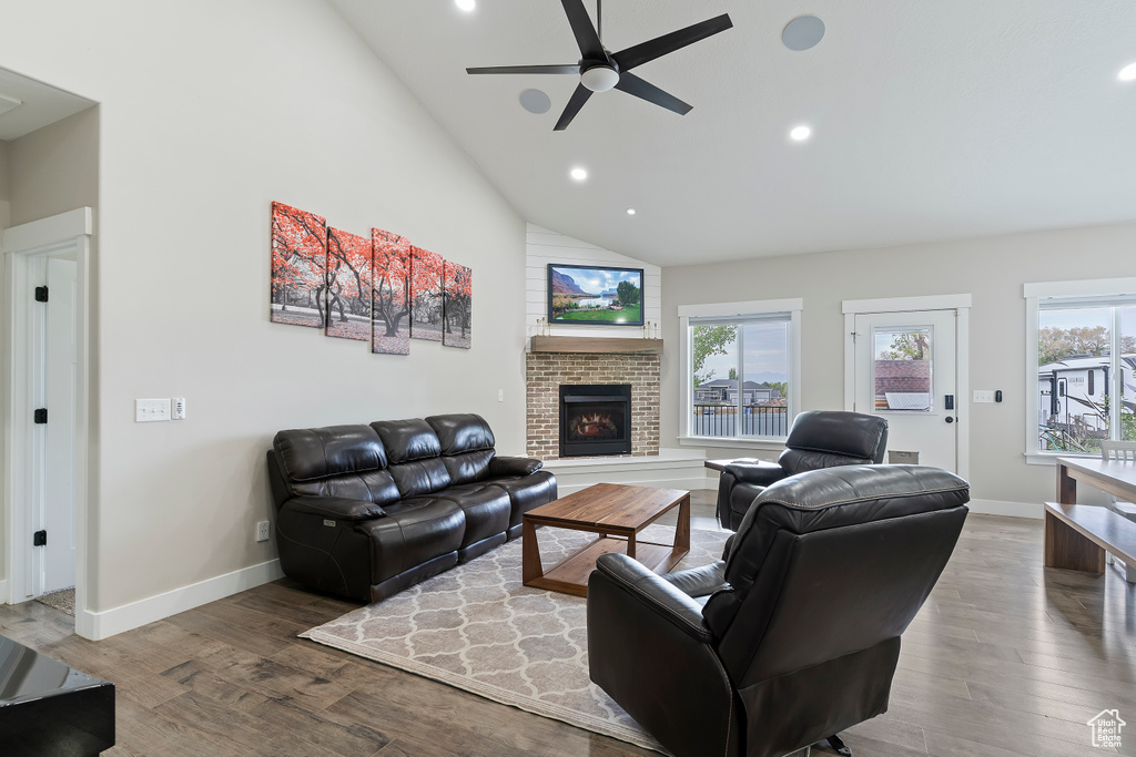 Living area with healthy amount of natural light, ceiling fan, high vaulted ceiling, wood finished floors, and a fireplace