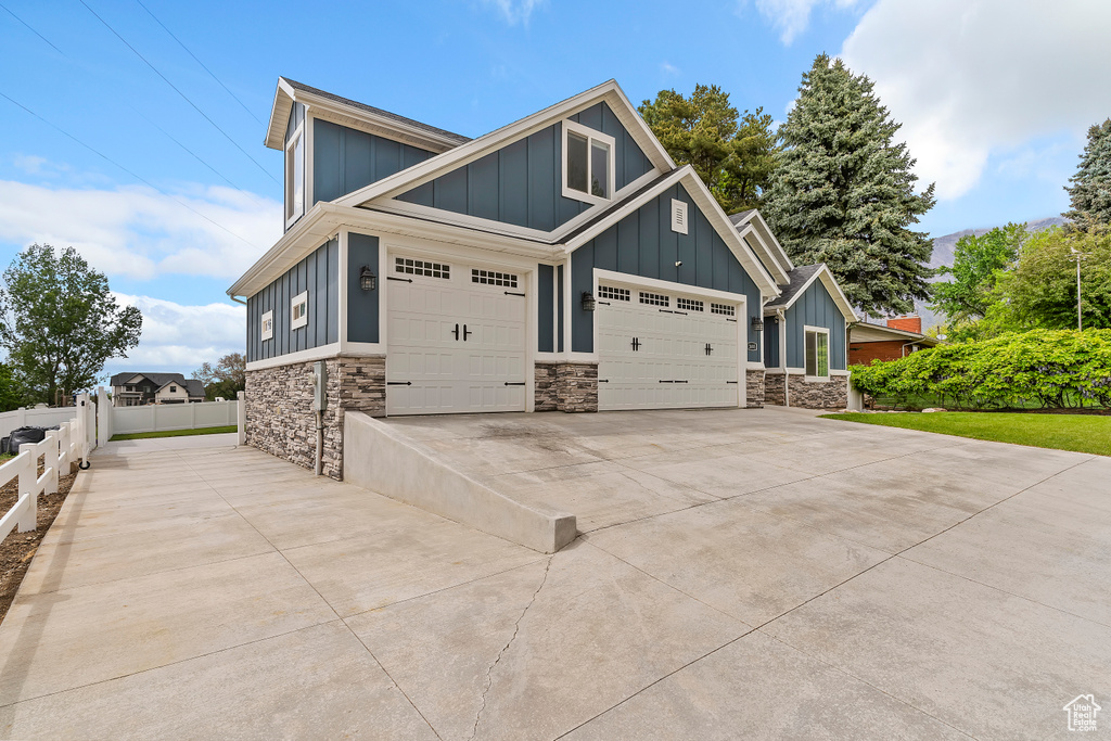 View of front facade with board and batten siding, stone siding, fence, and a garage