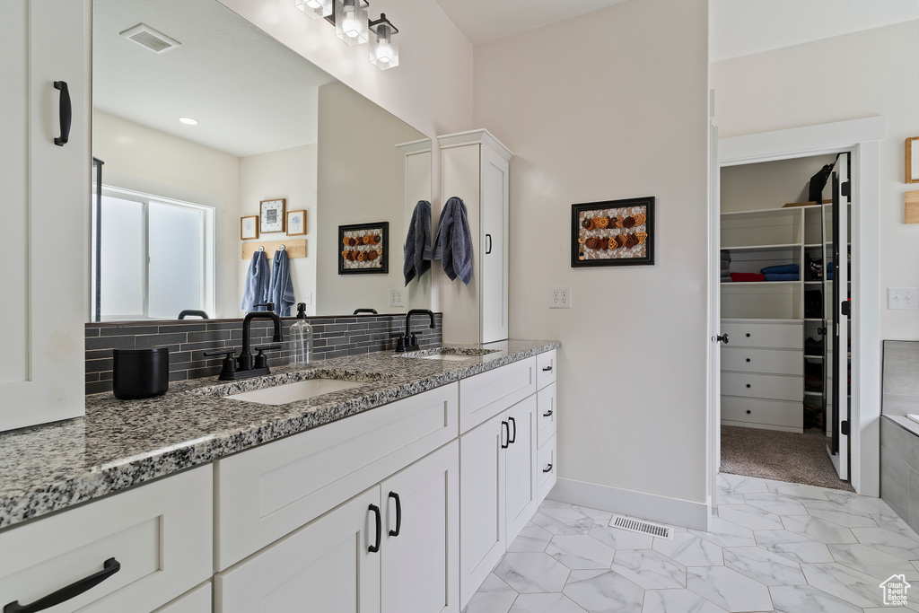 Bathroom featuring baseboards, double vanity, decorative backsplash, marble look tile flooring, and a spacious closet