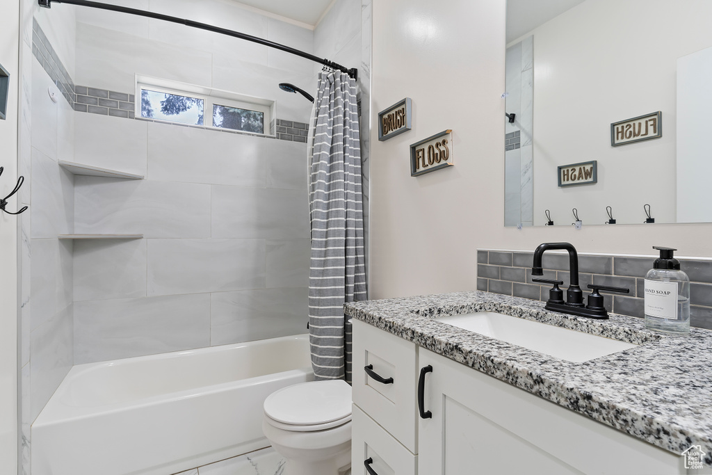 Bathroom featuring decorative backsplash, toilet, vanity, and shower / bath combo with shower curtain