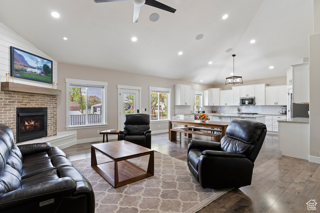 Living area with a ceiling fan, high vaulted ceiling, a fireplace, light wood-style flooring, and recessed lighting
