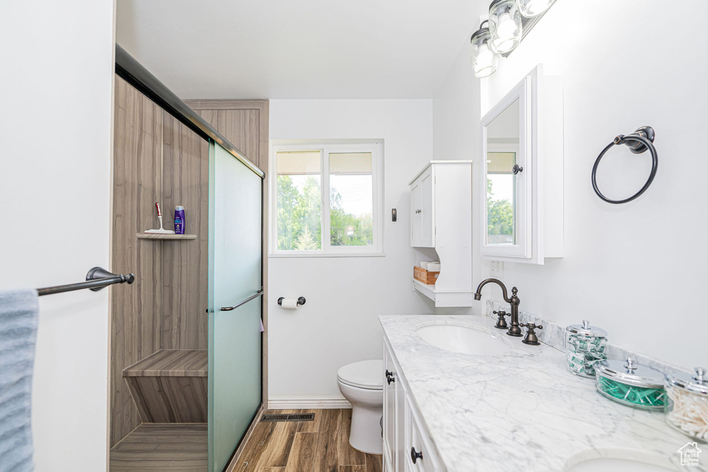 Full bathroom with a stall shower, wood finished floors, double vanity, and toilet