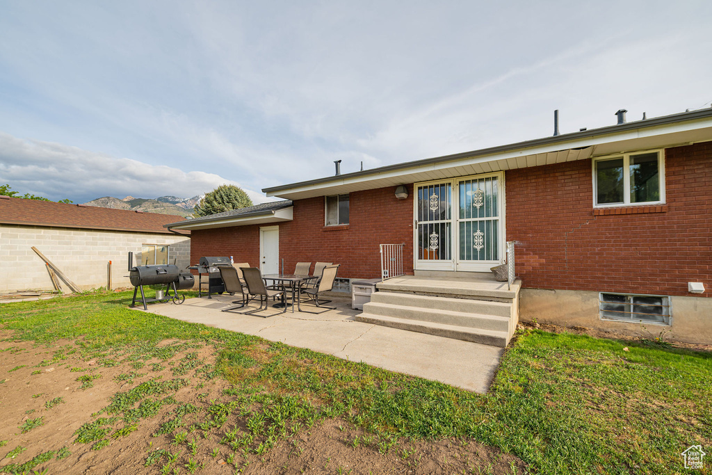 Rear view of property with brick siding, a patio area, a yard, and a mountain view