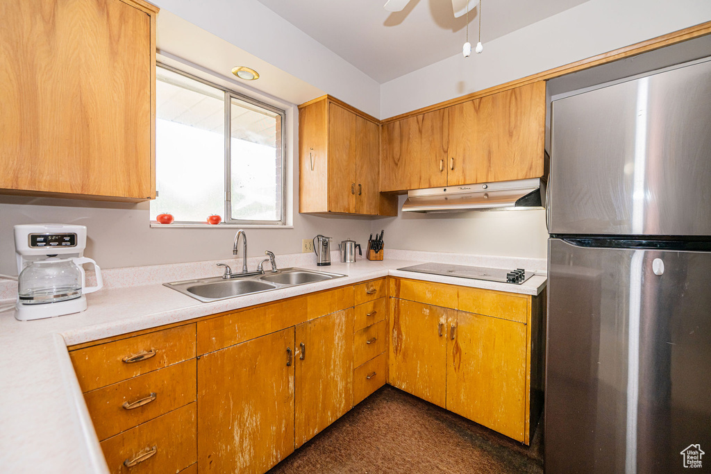 Kitchen featuring freestanding refrigerator, under cabinet range hood, a sink, electric cooktop, and light countertops