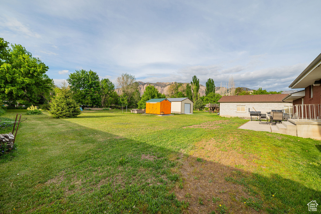 View of green lawn featuring a storage shed, a patio area, an outdoor structure, and a mountain view