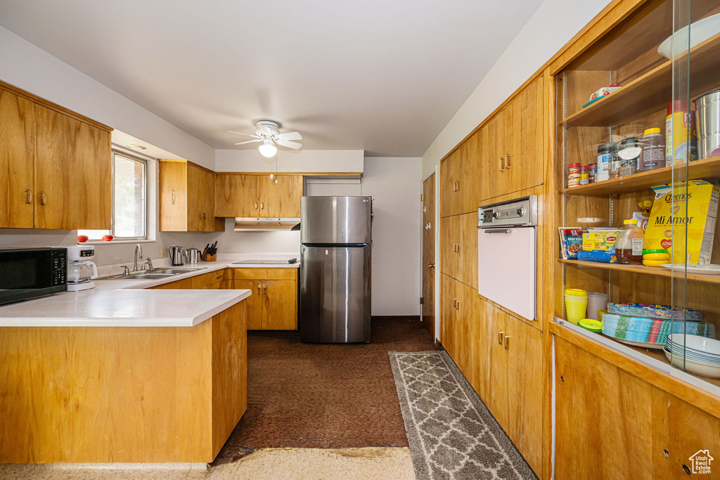 Kitchen with freestanding refrigerator, oven, black microwave, a ceiling fan, and a sink