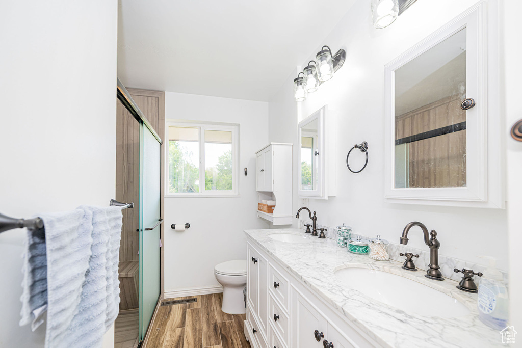 Full bath with double vanity, toilet, wood finished floors, a shower with shower door, and baseboards
