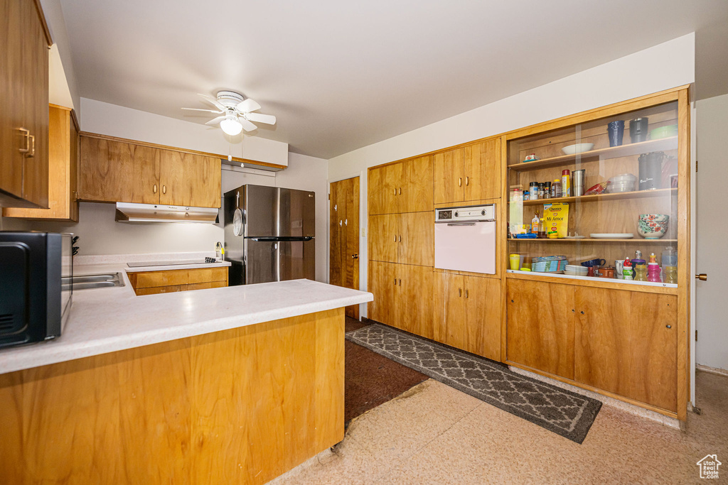 Kitchen with white oven, freestanding refrigerator, under cabinet range hood, ceiling fan, and tile patterned floors