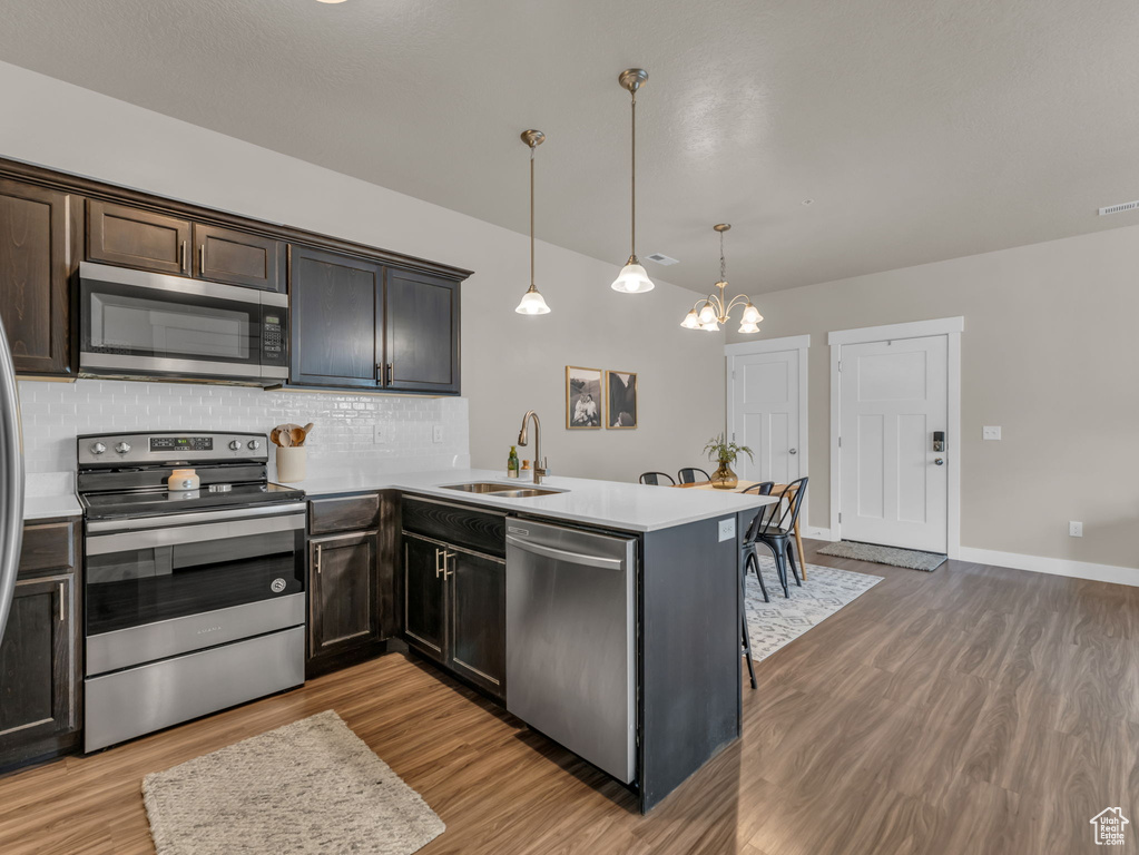 Kitchen with stainless steel appliances, a sink, light wood-type flooring, tasteful backsplash, and a peninsula