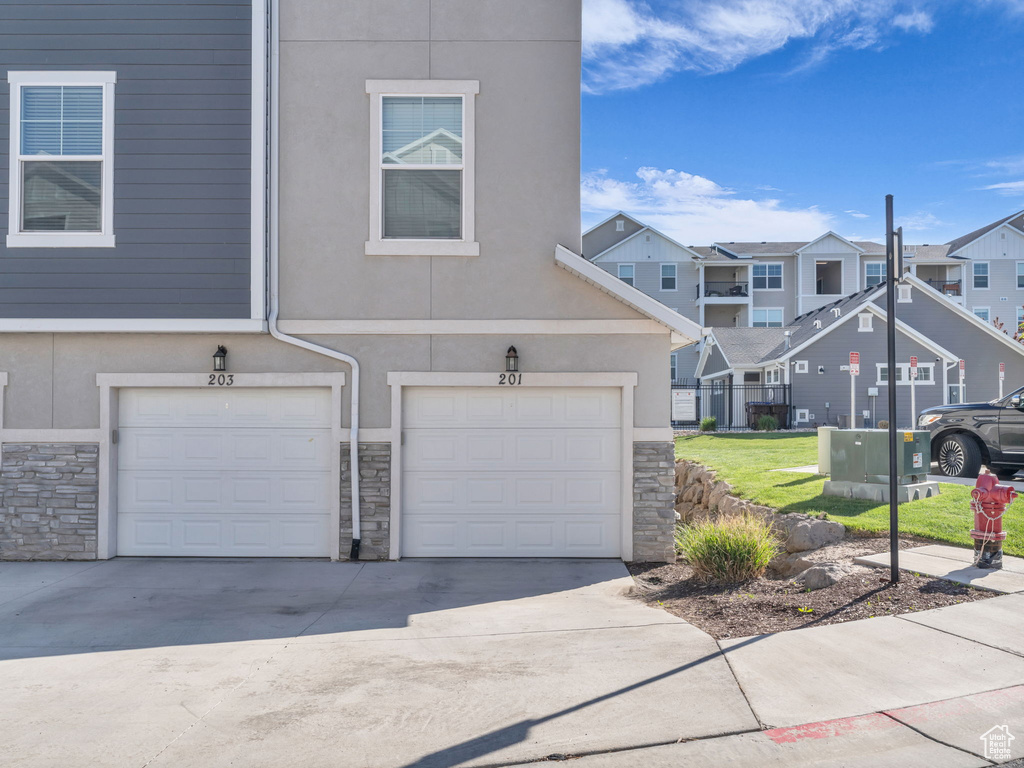 View of property with stone siding, a residential view, a garage, concrete driveway, and stucco siding