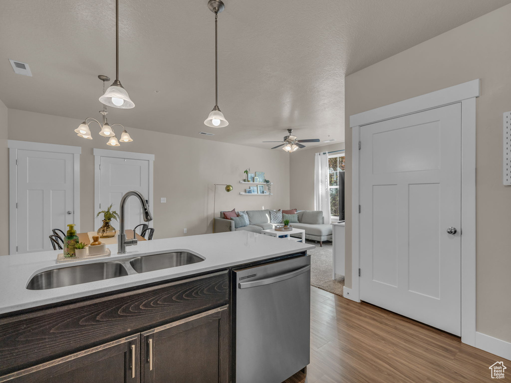 Kitchen with stainless steel dishwasher, a sink, dark brown cabinets, light wood-style floors, and pendant lighting
