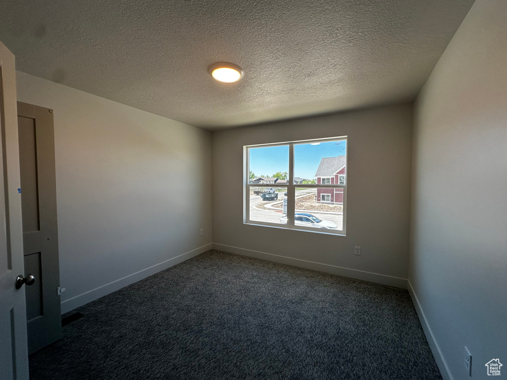 Empty room featuring carpet, a textured ceiling, and baseboards
