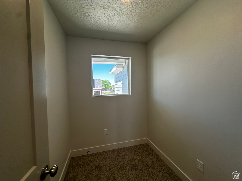 Spare room with dark colored carpet, baseboards, and a textured ceiling