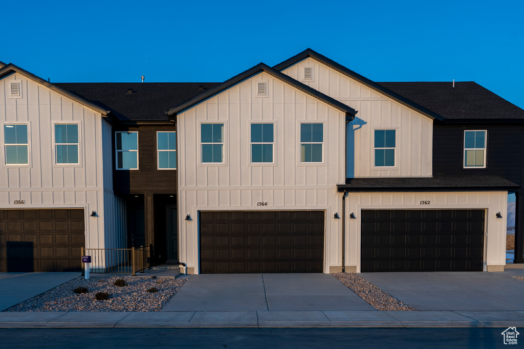 View of front of home featuring board and batten siding, an attached garage, concrete driveway, and a shingled roof