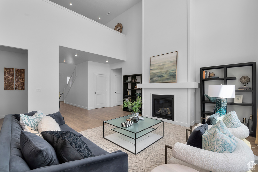 Living room with wood finished floors, a towering ceiling, a glass covered fireplace, baseboards, and recessed lighting