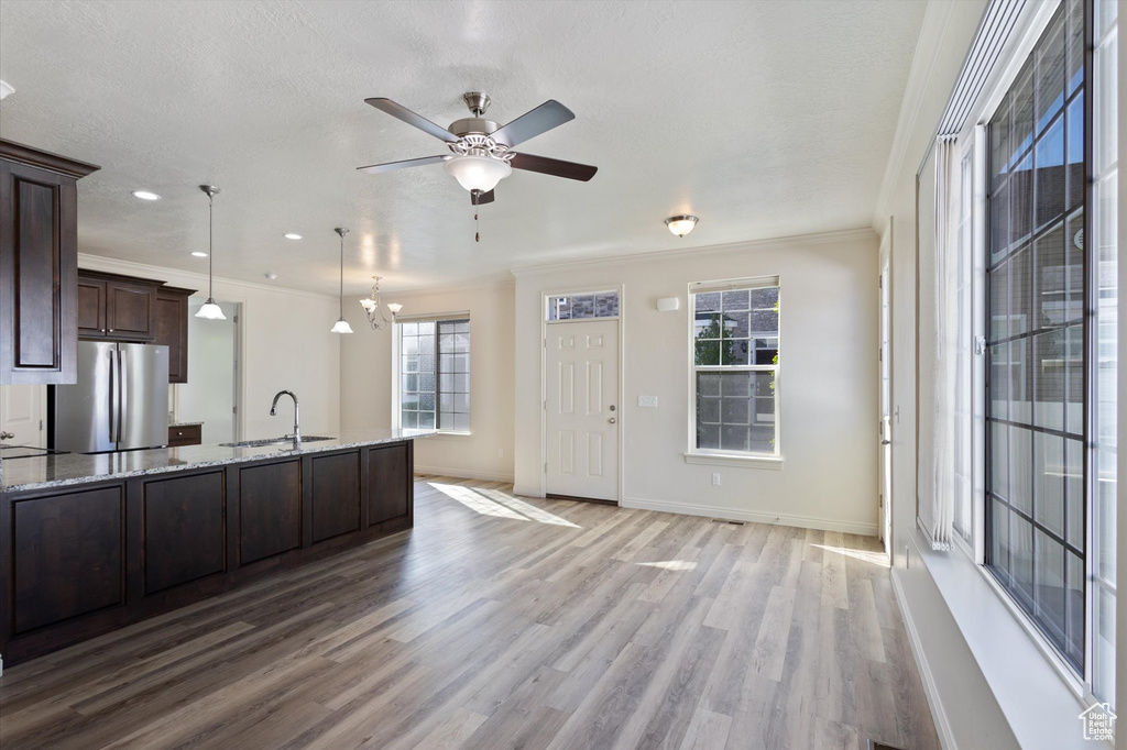Kitchen featuring freestanding refrigerator, a sink, dark brown cabinets, wood finished floors, and light stone counters