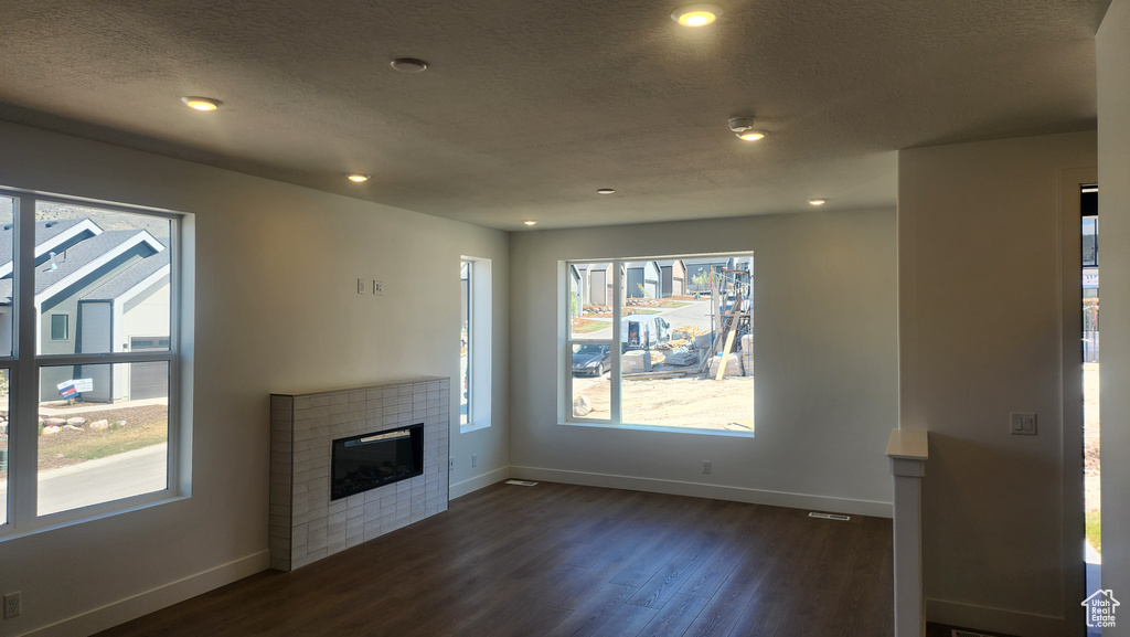 Unfurnished living room with baseboards, dark wood finished floors, a tiled fireplace, and recessed lighting