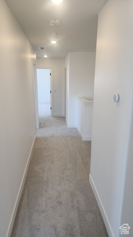 Hallway featuring light colored carpet and baseboards