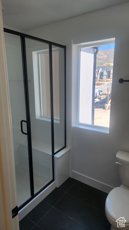 Bathroom featuring tile patterned flooring, toilet, a shower stall, and healthy amount of natural light