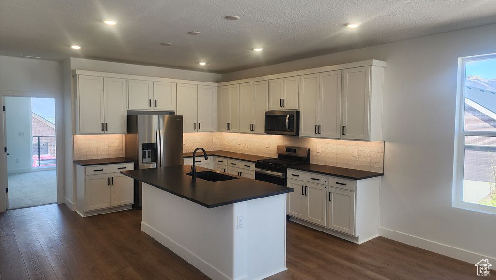 Kitchen with appliances with stainless steel finishes, a sink, dark countertops, dark wood-style flooring, and recessed lighting