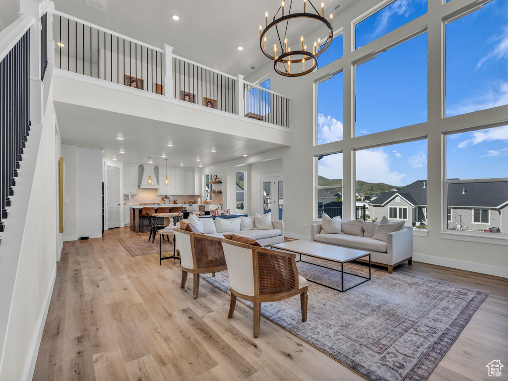 Living room with a high ceiling, baseboards, light wood-type flooring, a chandelier, and recessed lighting