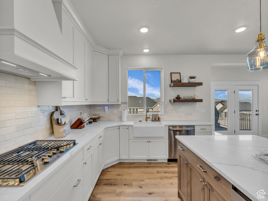 Kitchen featuring appliances with stainless steel finishes, premium range hood, a sink, light wood finished floors, and backsplash