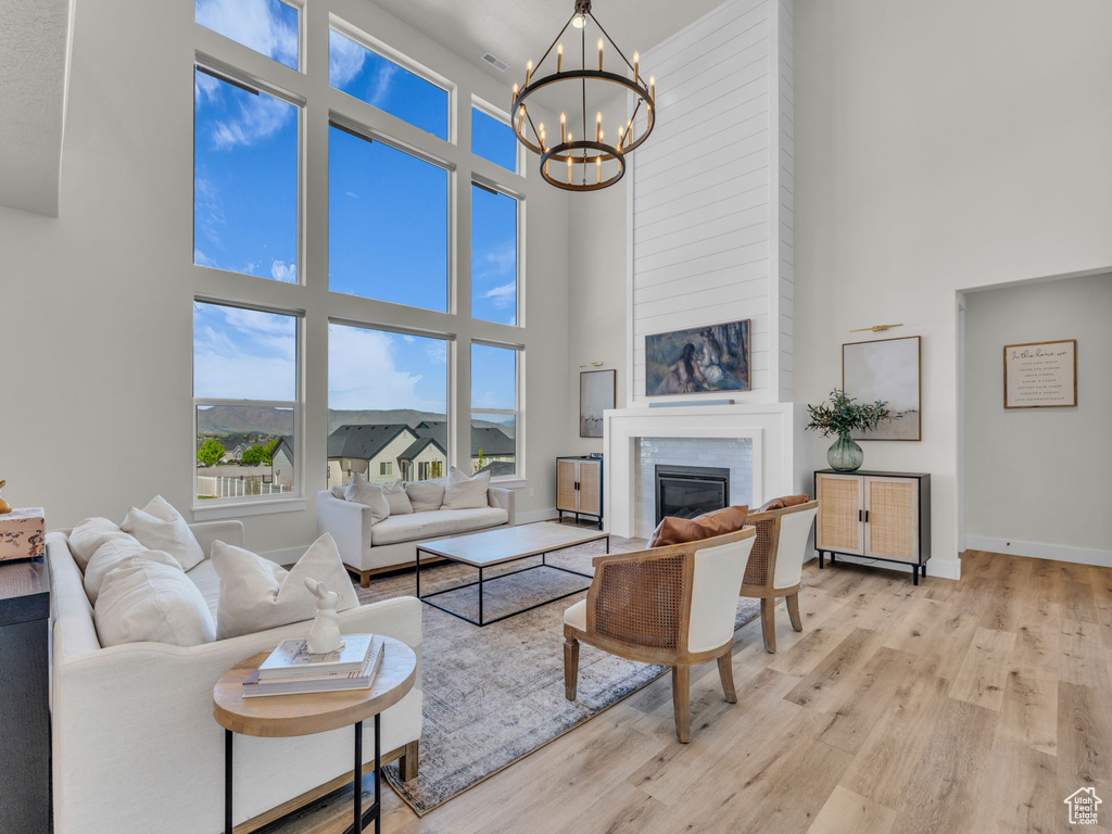Living area featuring a high ceiling, a chandelier, a large fireplace, wood finished floors, and baseboards
