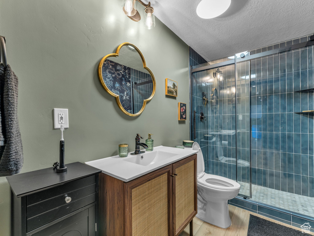 Full bath featuring a shower stall, vanity, a textured ceiling, toilet, and wood finished floors