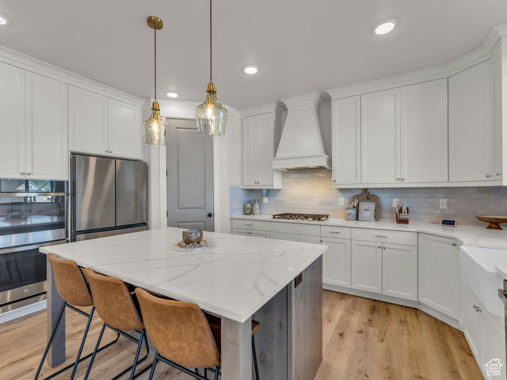 Kitchen with premium range hood, appliances with stainless steel finishes, a kitchen island, decorative backsplash, and white cabinets