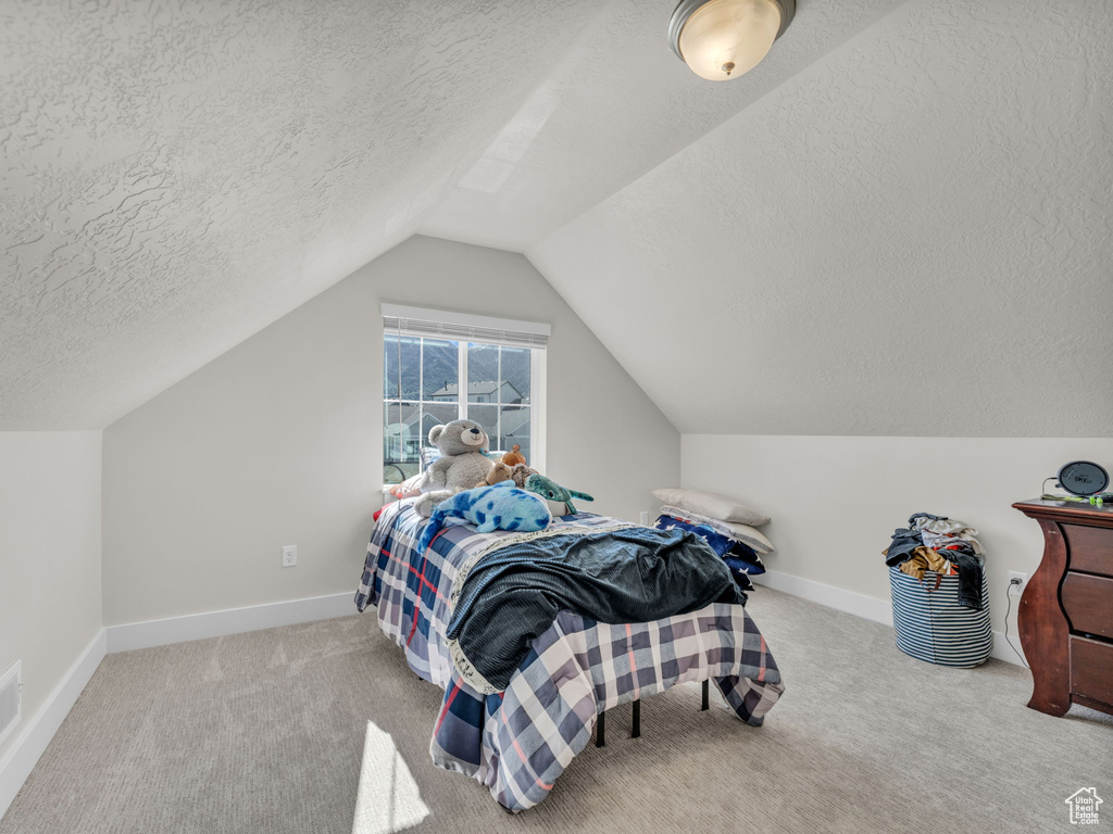 Bedroom with a textured ceiling, lofted ceiling, carpet flooring, and baseboards