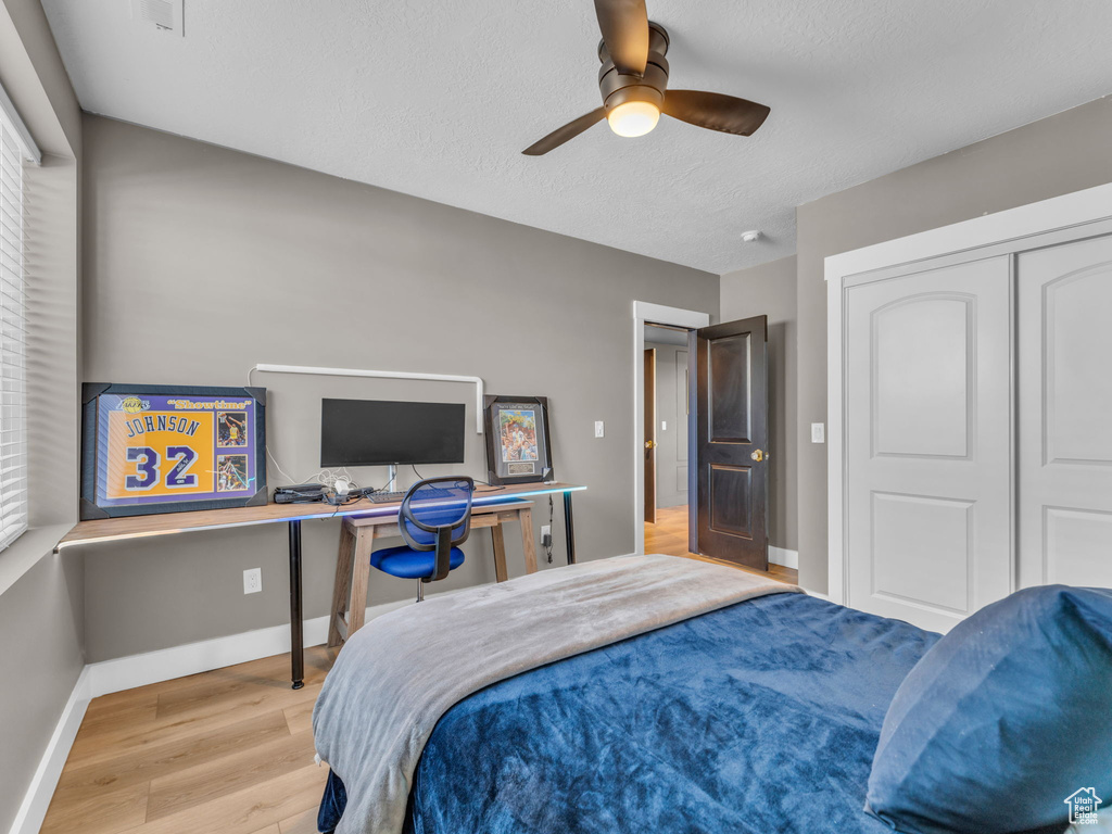 Bedroom with wood finished floors, an office area, baseboards, a ceiling fan, and a closet