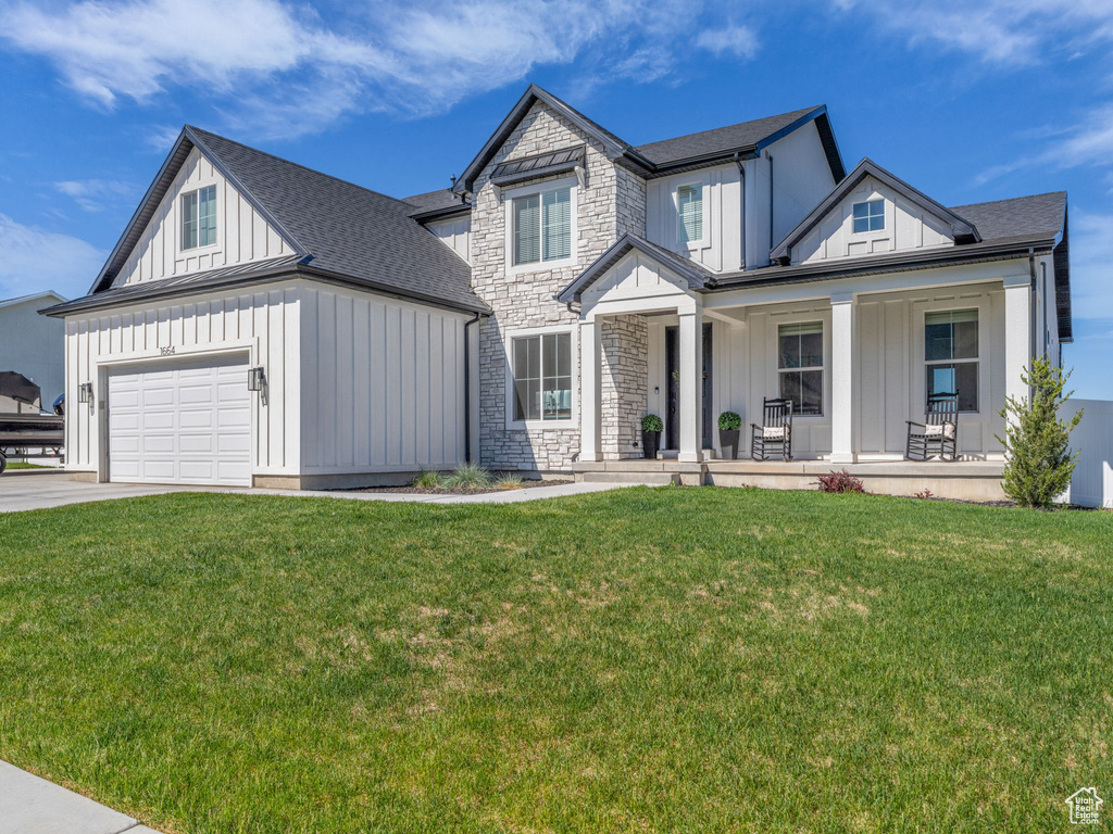 View of front of property with board and batten siding, covered porch, a garage, driveway, and a front lawn