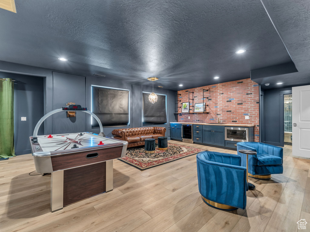Recreation room with a textured ceiling, light wood-style flooring, wine cooler, recessed lighting, and a sink