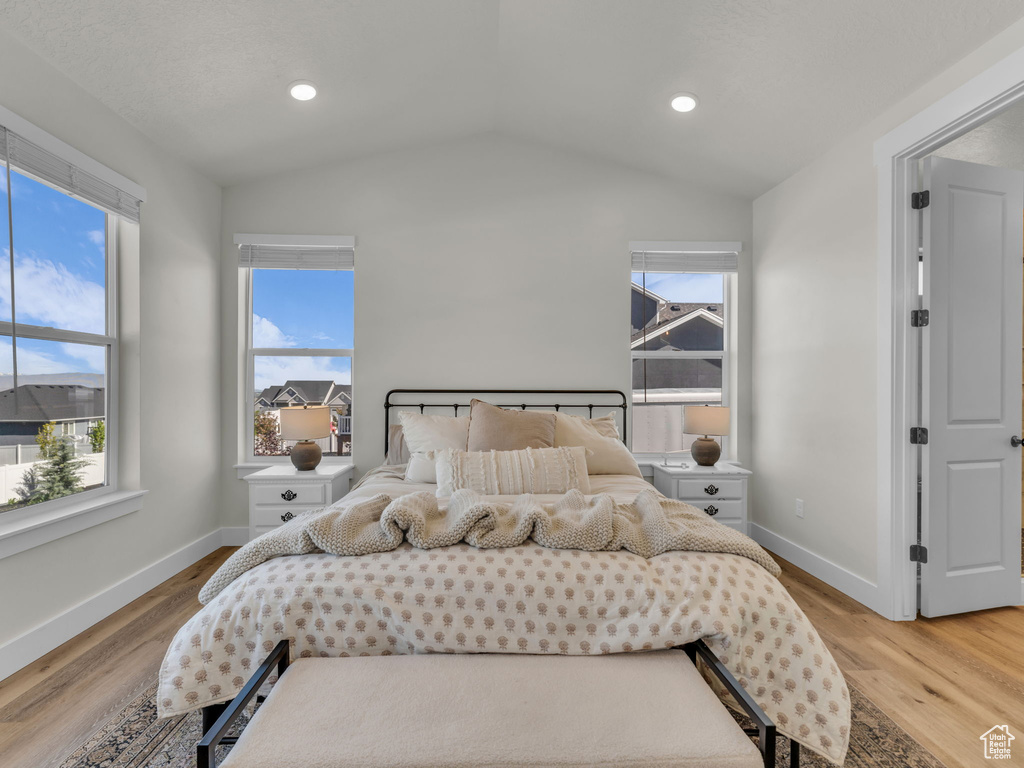 Bedroom with vaulted ceiling, baseboards, light wood-style floors, multiple windows, and recessed lighting
