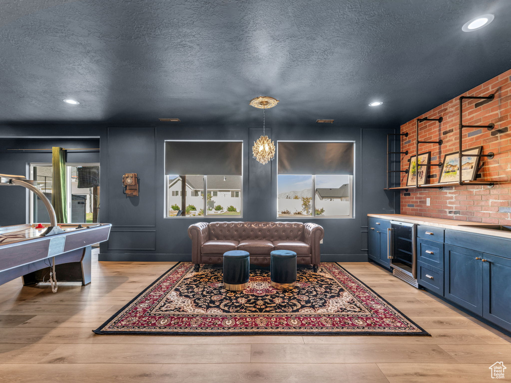 Living area featuring wine cooler, light wood finished floors, a bar, a textured ceiling, and recessed lighting