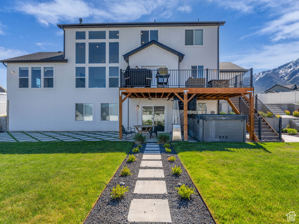 Back of house with stucco siding, stairway, a deck with mountain view, a patio, and a lawn