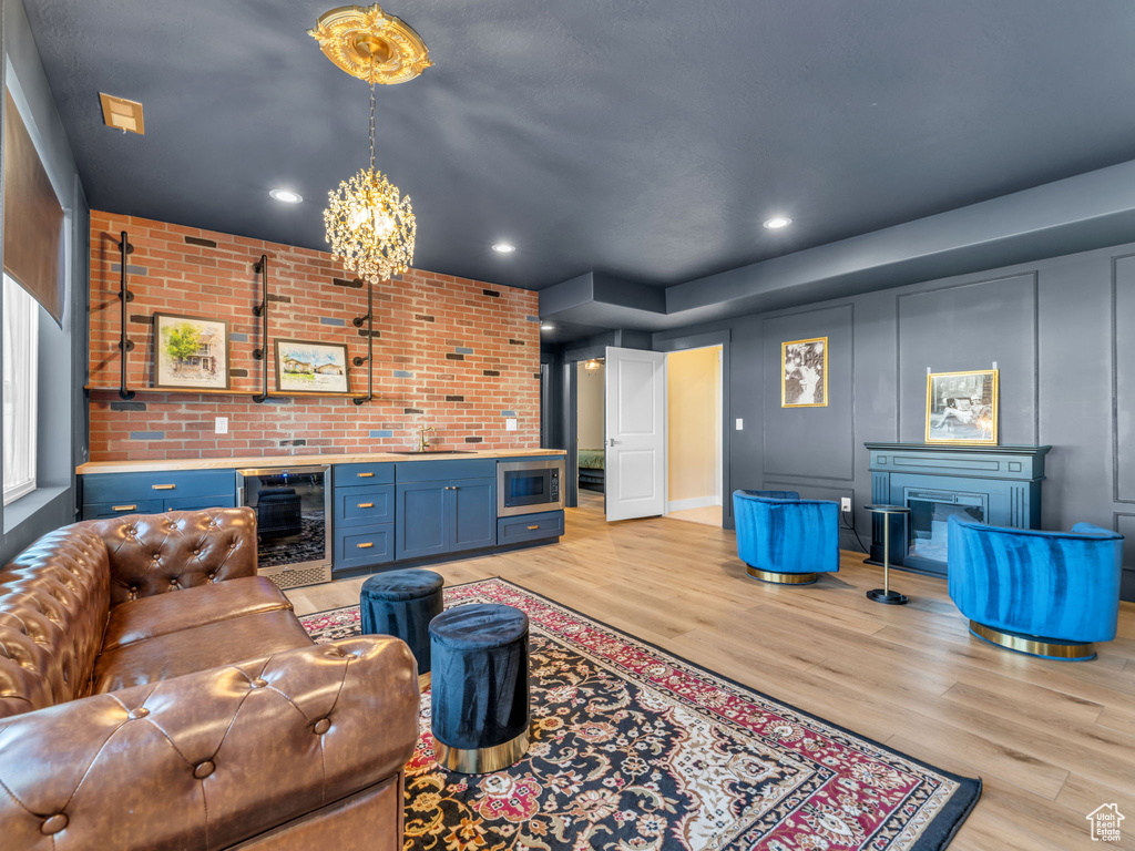 Living area with beverage cooler, a fireplace, light wood finished floors, a chandelier, and brick wall