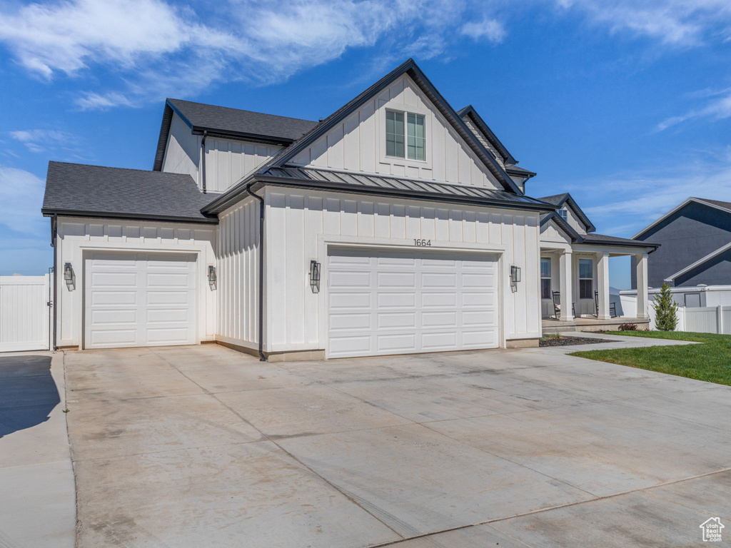 Modern farmhouse featuring driveway, a standing seam roof, a garage, and fence