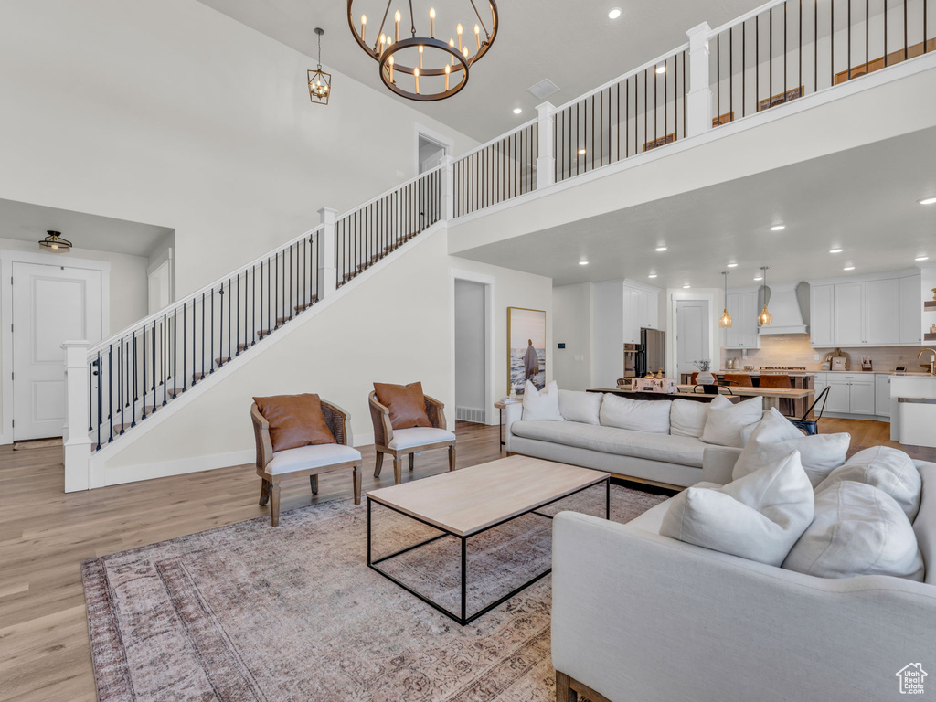Living area featuring a high ceiling, light wood-type flooring, stairs, a chandelier, and baseboards