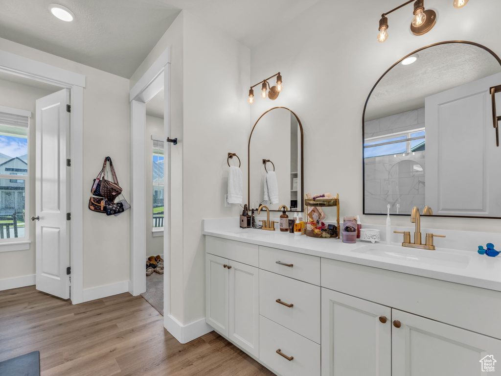 Bathroom featuring wood finished floors, double vanity, baseboards, and a shower