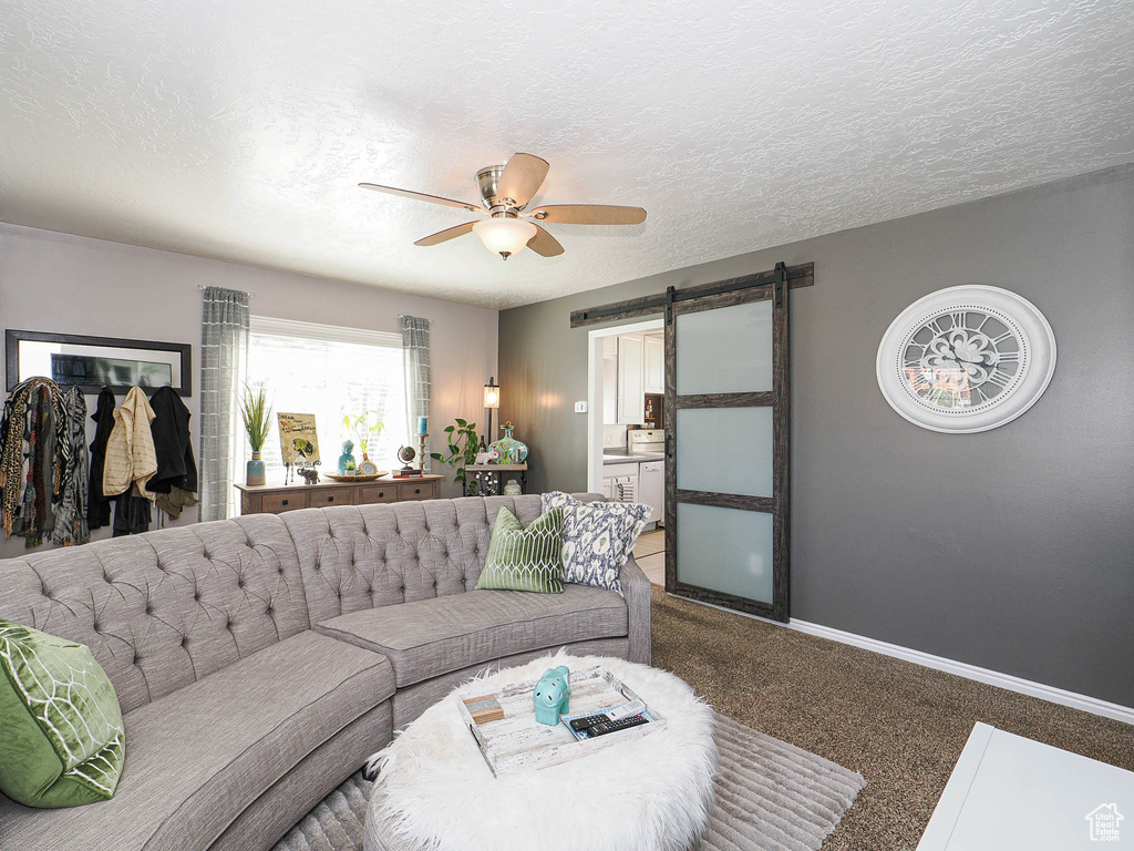 Living area with a barn door, a ceiling fan, carpet, baseboards, and a textured ceiling