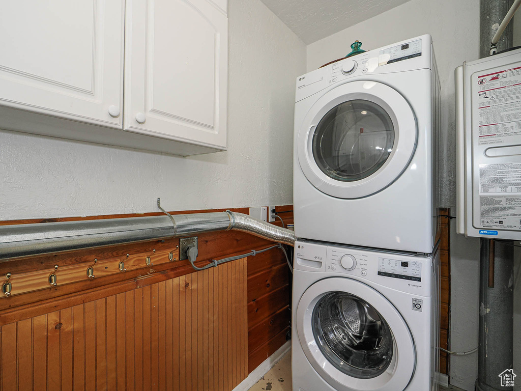 Clothes washing area with estacked washer and dryer, cabinet space, and water heater