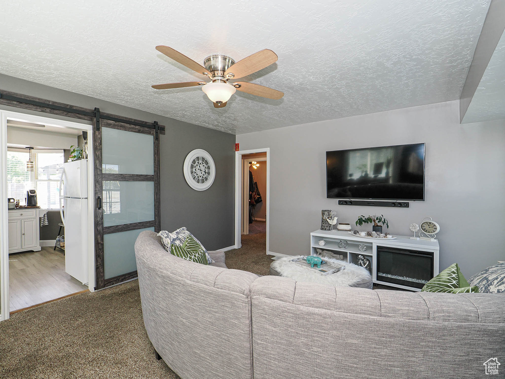 Living area featuring ceiling fan, a textured ceiling, carpet floors, baseboards, and a barn door