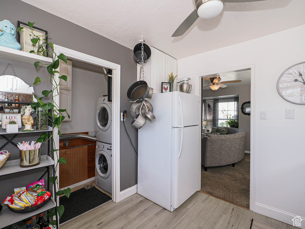 Washroom with stacked washer / drying machine, a ceiling fan, and light wood-type flooring
