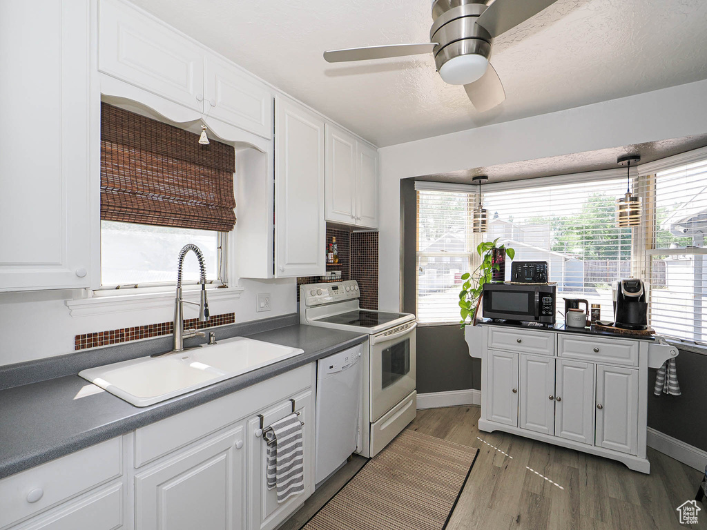 Kitchen featuring white appliances, a sink, dark countertops, white cabinetry, and light wood finished floors