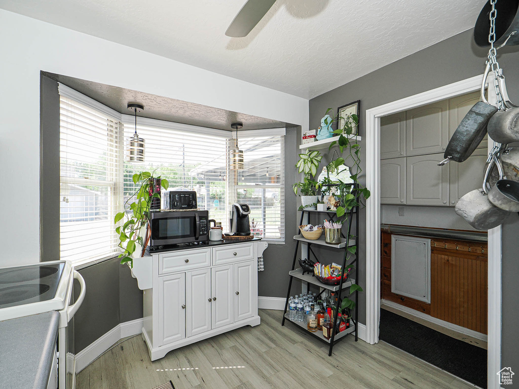 Kitchen featuring black microwave, light wood-type flooring, white cabinets, ceiling fan, and baseboards