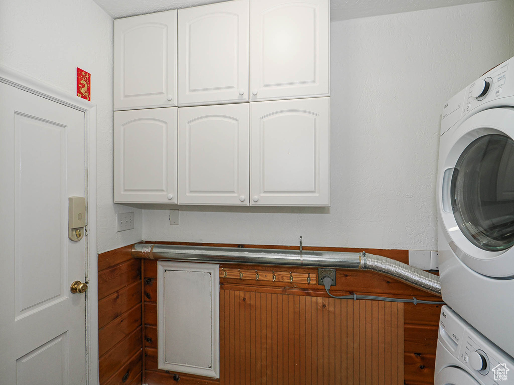 Clothes washing area featuring stacked washer / drying machine and cabinet space