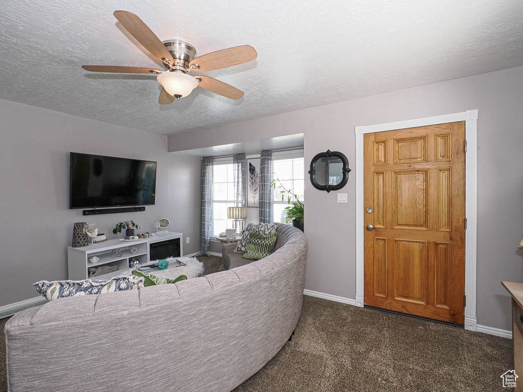 Living area with a textured ceiling, carpet floors, a ceiling fan, and baseboards