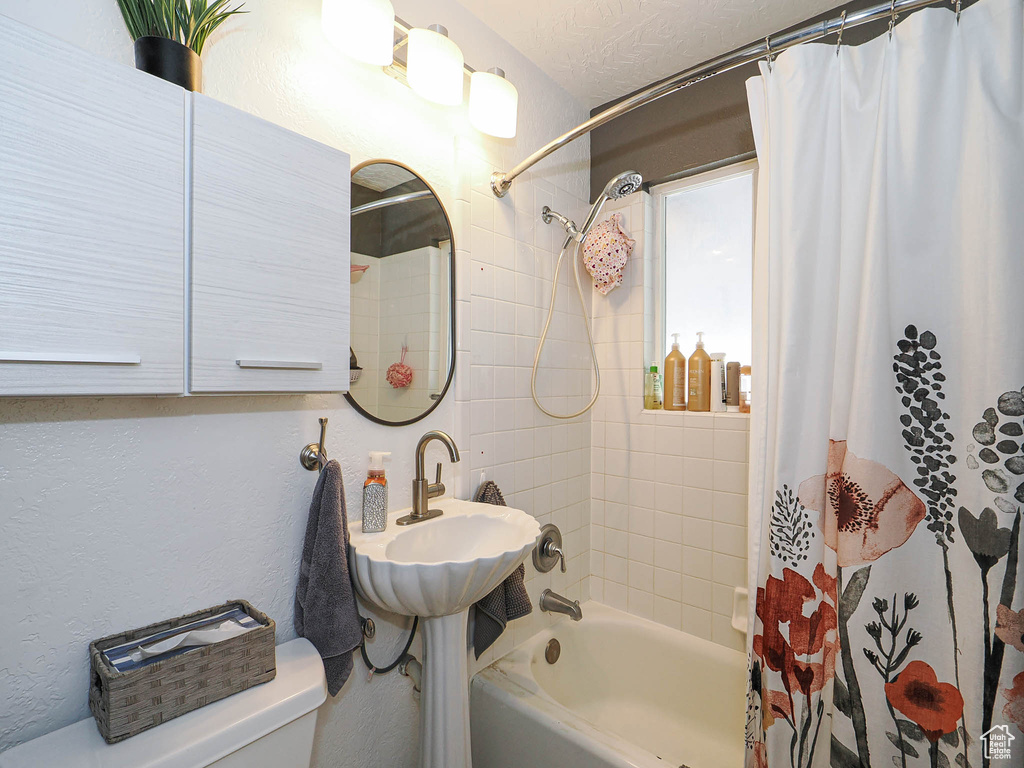 Full bath with shower / tub combo, toilet, and a textured wall